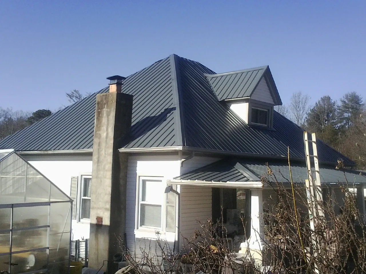 Dark blue standing seam metal roof on a white farmhouse with dormer — Slate & Tile Roof Repair by Roofing Brothers in Cascadia