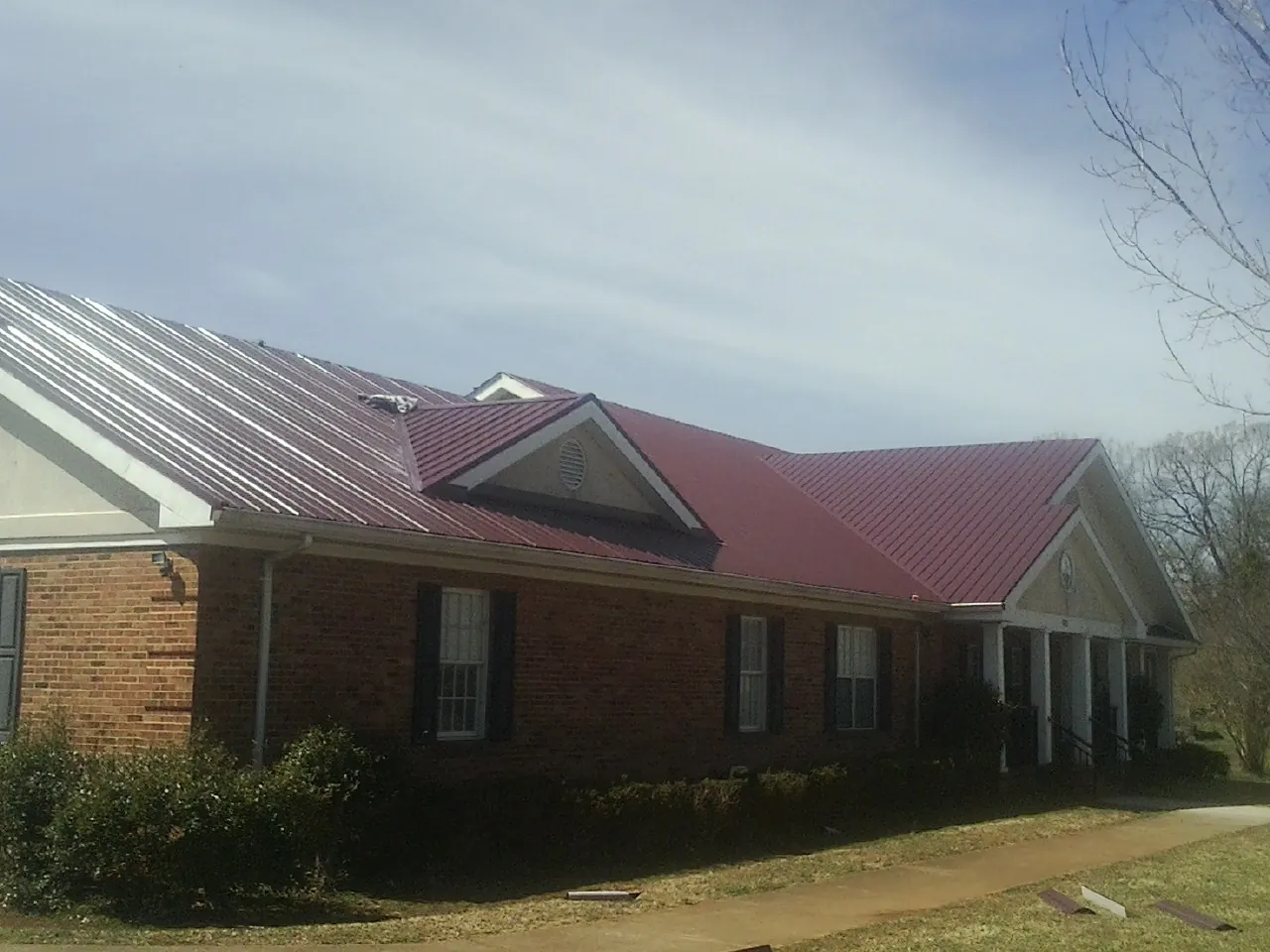Red metal roof with gabled entries on a long brick building, from a Hail Damage Roof Repair job in Cascadia