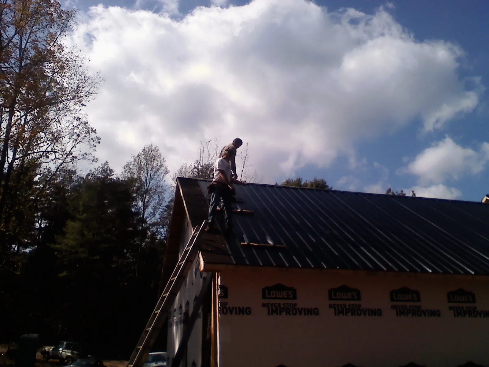 Roofer fastening dark metal panels high against a cloudy sky, from a Roof Inspection job in Cascadia