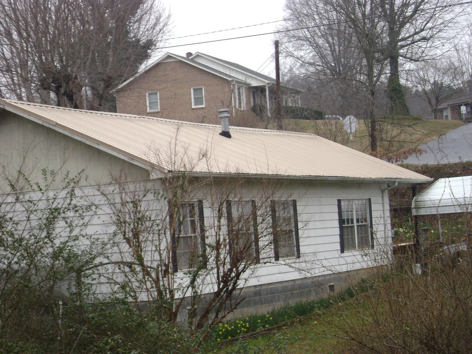Tan metal roof on a white sided house set into a hillside — Commercial Roofing by Roofing Brothers in Cascadia
